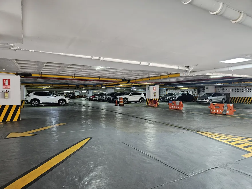 Nivel del estacionamiento del hotel, techado e iluminado, con coches estacionados y las guías pintadas en amarillo