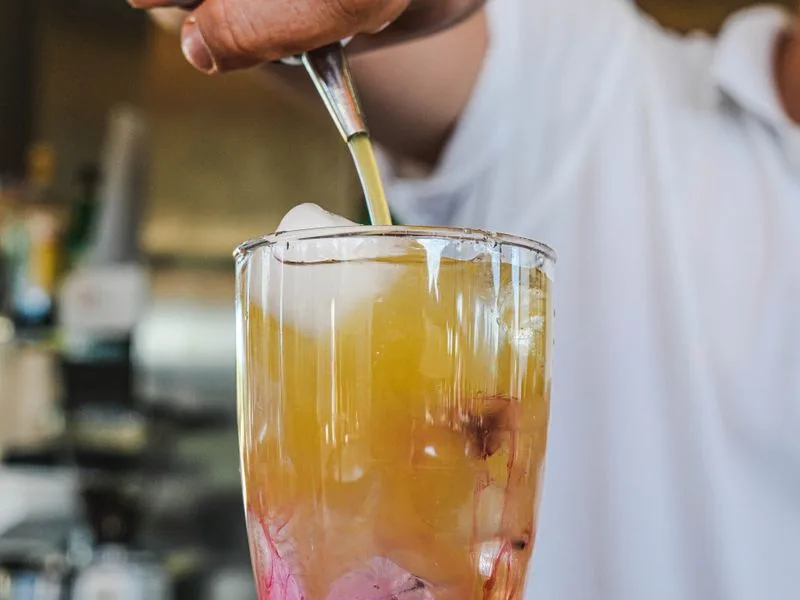 Imagen de referencia: cu{00F3}ctel de capas naranjas y rojas serviu{00E9}ndose en un vaso alto con hielo