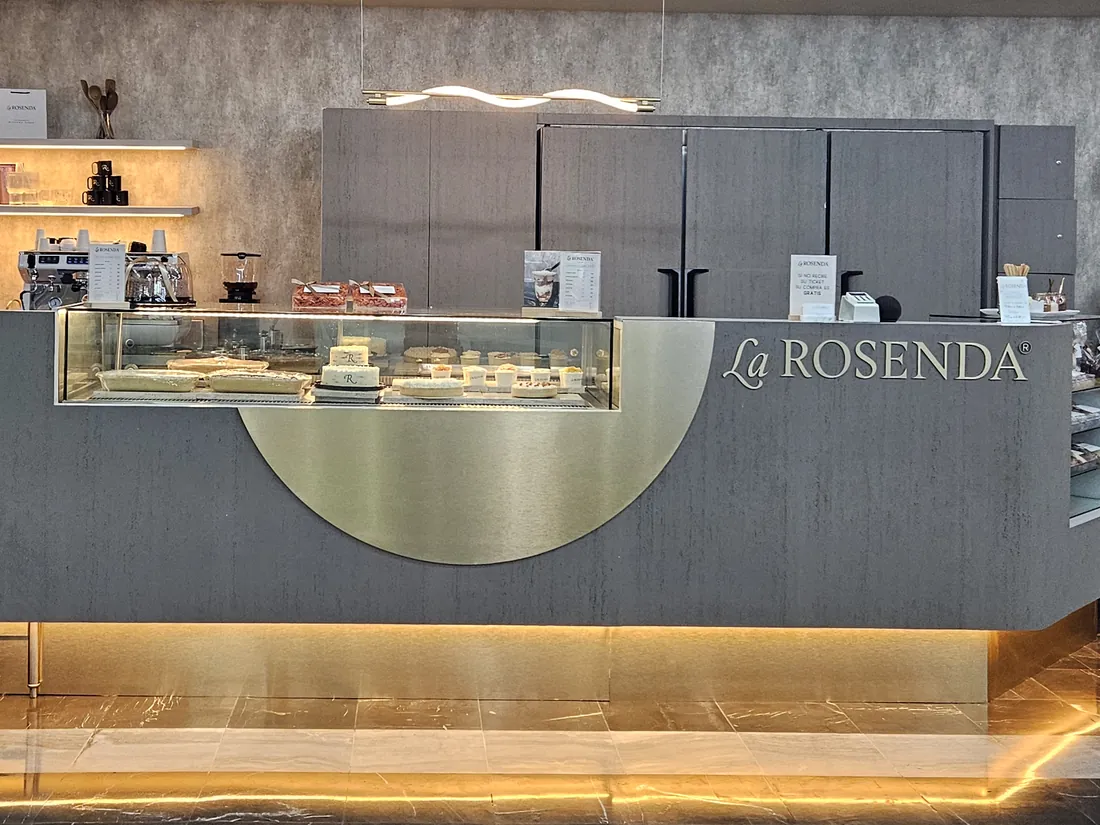 Mostrador de La Rosenda: la vitrina de pasteles, el frente dorado iluminado y el nombre de la casa sobre la barra