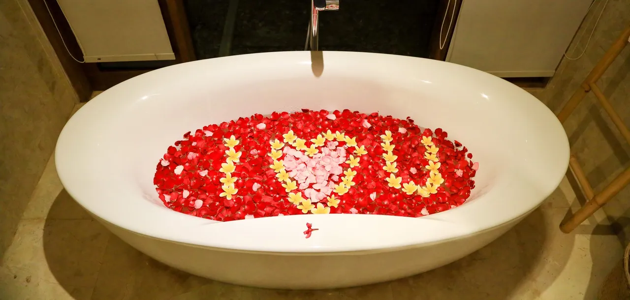Tina ovalada llena de pétalos rojos y flores amarillas que forman un corazón, preparada para el paquete Luna Mielero